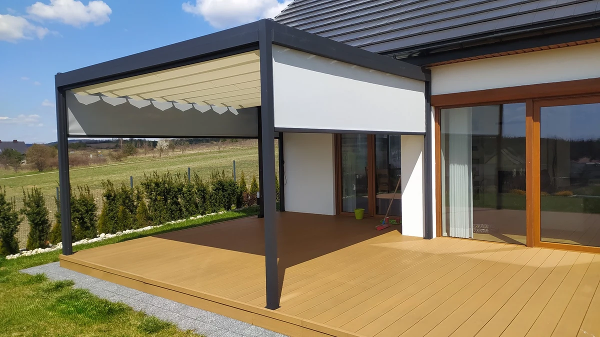 Pergola tarasowa w kolorze antracytowym z jasnym zadaszeniem i osłonami bocznymi przy domu